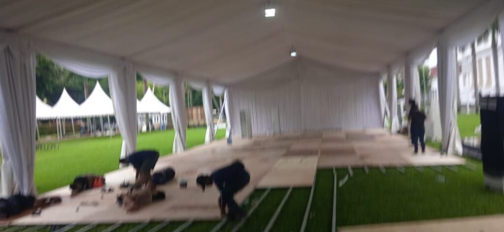 Tenda roder putih dengan dekorasi bunga sedang dipasang di pantai.